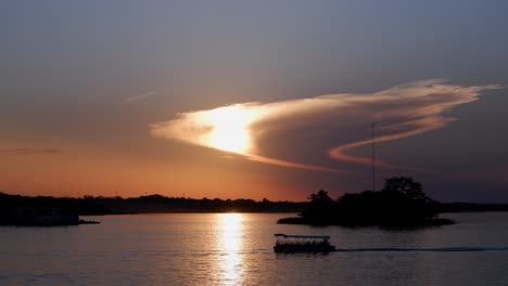 pontoon boat motors through sunset sun beam on golden lake water