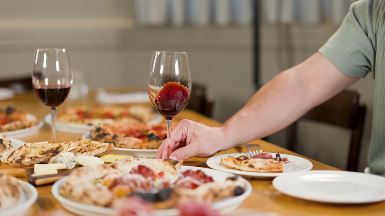 Persona che fa roteare vino rosso nel bicchiere a tavola con pizza