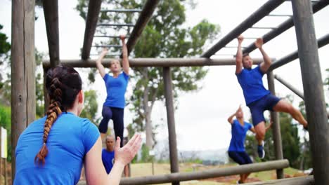 Female-trainer-clapping-hands-while-fit-people-climbing-monkey-bars-4k