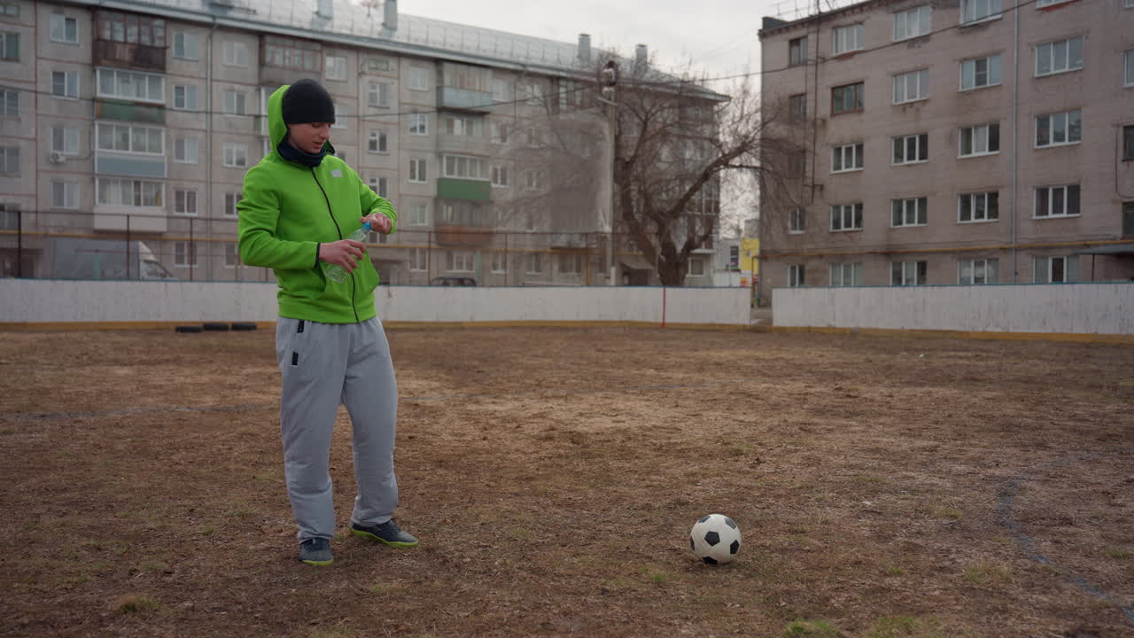 Hombre caucásico entrenando solo en un campo urbano vacío, con actitud contemplativa y respiración constante, campo agreste y bloque de apartamentos al fondo, centrado en la repetición, la resiliencia y la silenciosa determinación.