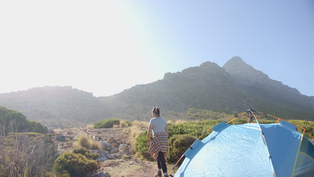 Hiking in mountains, woman walking near blue tent on sunny day, copy space