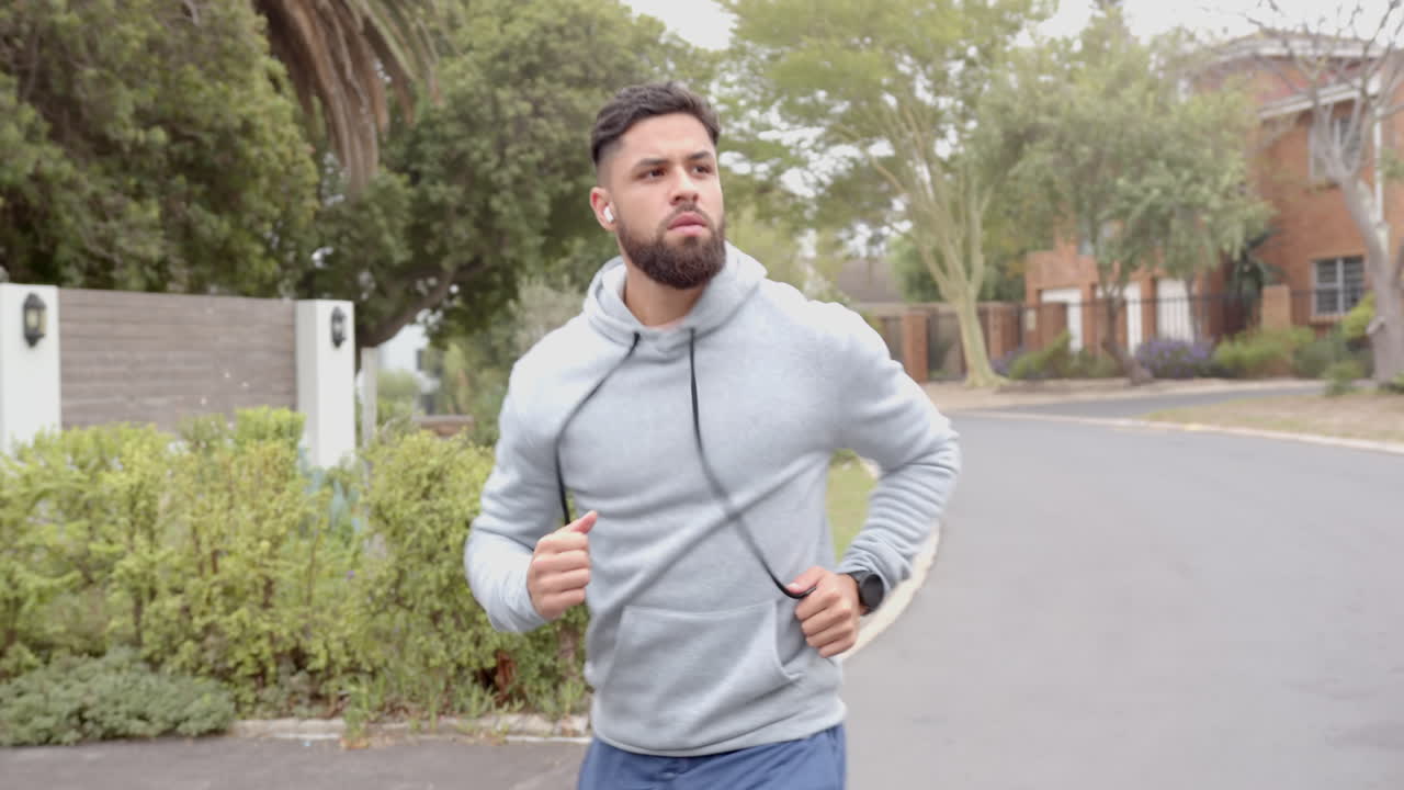 Jogging outdoors, man in hoodie exercising with smartwatch in neighborhood