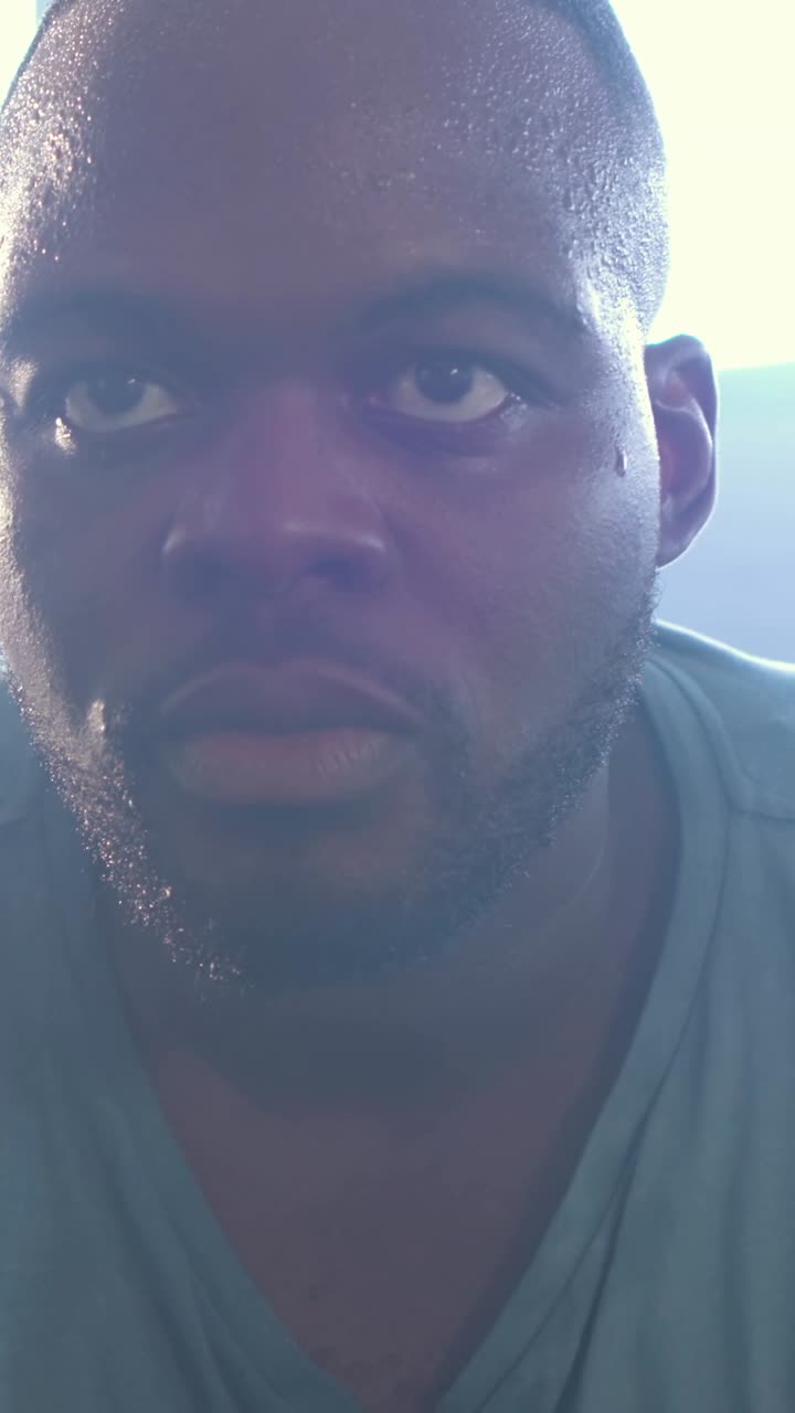 Vertical video: Pulling back camera, man shifting eyes for framing at window, sweating in light tee