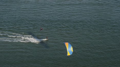 a dynamic tracking aerial footage of kitesurfers giving into the wind going steady while the other one changes direction and jumps into the air doing a back flip to avoid contact against the other one