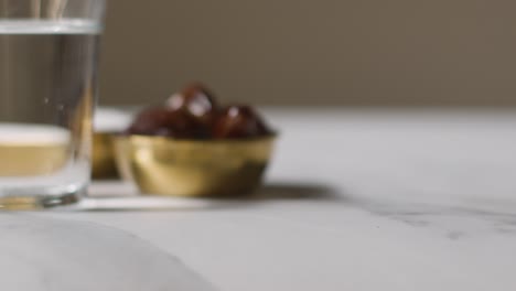 primo piano della ciotola di datteri con zucchero e bicchiere d'acqua sulla superficie di marmo che celebra la festa musulmana di eid