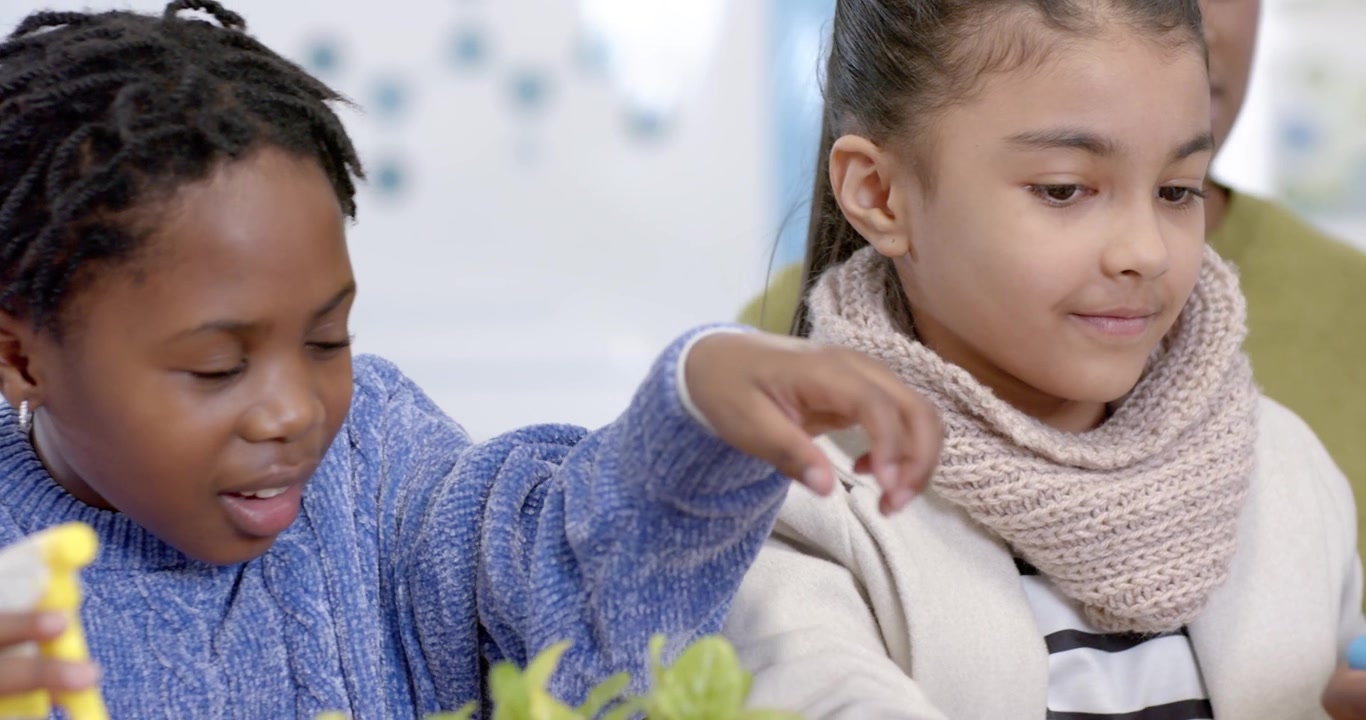 Afroamerikanische Kinder pflegen Setzlinge an einem Schultisch mit Hilfe der Lehrkraft, eine Sprühflasche benutzend.