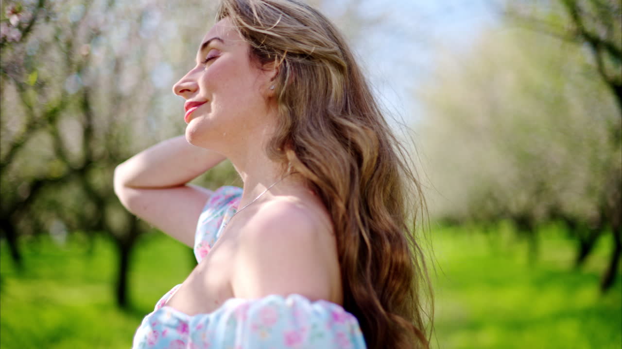 Brunette woman in a blue dress enjoying a field of blooming almond trees