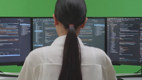 woman programmer coding on two monitors