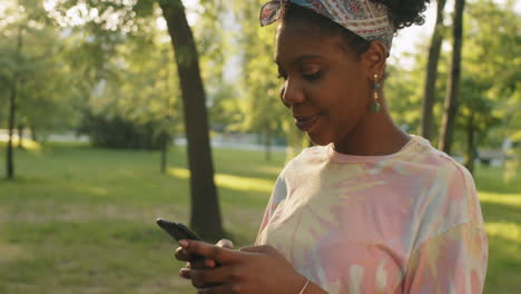 Alegre-Mujer-Afroamericana-Usando-Teléfono-Inteligente-Al-Aire-Libre