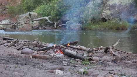 a camp fire burning away on the shores of a river bank in the australian bush