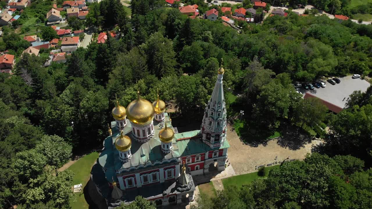 шипкинская мемориальная церковь в болгарии - красивая церковь с разноцветными экстерьерами и золотыми куполами на фоне пышной зелени деревьев - съемка с беспилотника
