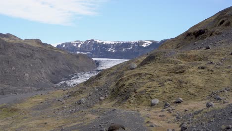 Icelandic-landscape-with-glacier-between-mountains,-green-moss-covered-hills-under-blue-sky