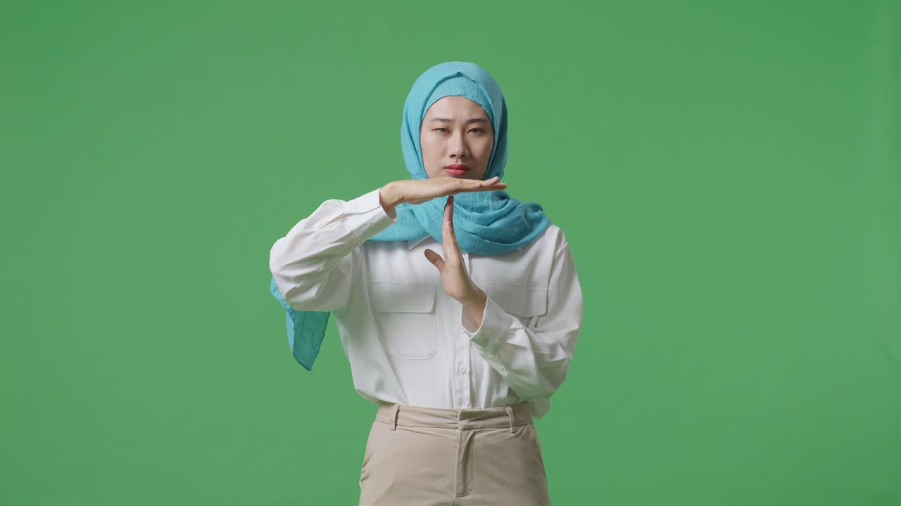 mujer musulmana mirando a la cámara y mostrando el gesto del tiempo de espera mientras está de pie en el estudio de fondo de la pantalla verde
