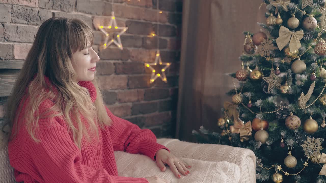 예쁜 여자가 장식된 크리스마스 트리 근처 소파에 포즈를 취하다