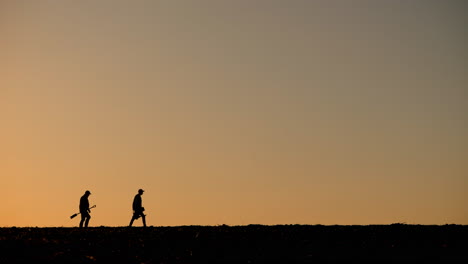 silueta de agricultores trabajando en el campo al atardecer