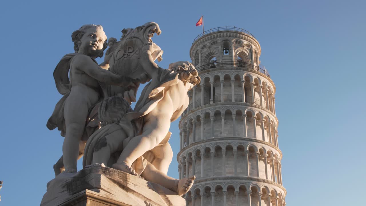cerca de la torre inclinada de pisa con un cielo azul claro en la mañana durante la hora dorada con una estatua en primer plano filmada con un cardán y un movimiento de muñecas en toscana, italia