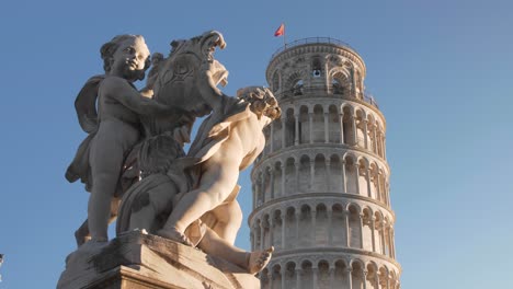 close up of the leaning tower of pisa with clear blue sky in the morning during golden hour with statue in the foreground filmed with a gimbal and a dolly movement in tuscany, italy