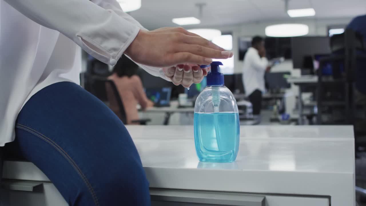 sección media de la mujer desinfectando sus manos en la oficina