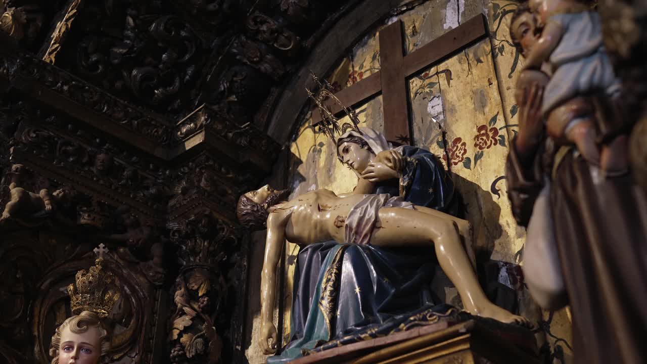 Religious sculpture depicting the Pietà, with the Virgin Mary holding the lifeless body of Jesus, set against an ornate and aged church interior
