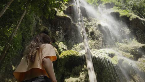 tilt up to woman in crop top looking at cascading mist of water falling in tropical jungle