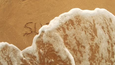 surfing lettering on the warm sand washes away the sea water on a sunny day.