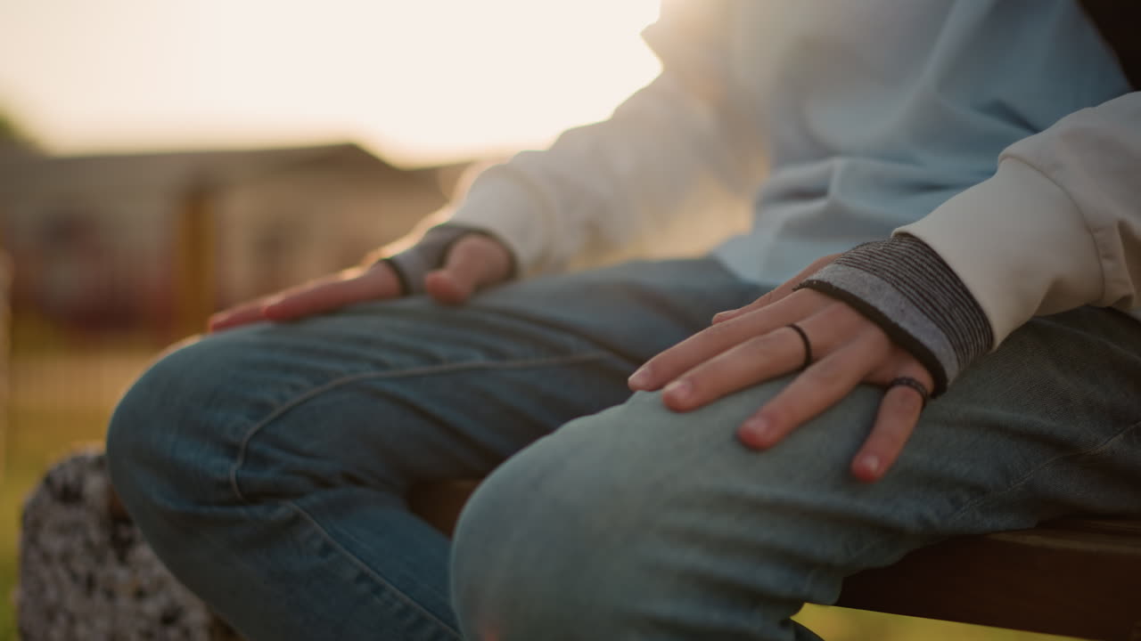 Dita che si agitano leggermente sotto una luce calda. Mani calme che riposano mentre le ombre della sera appaiono dolcemente. Postura delicata con le mani appoggiate sul ginocchio in mezzo alla luce solare che svanisce e alla tranquilla anticipazione.
