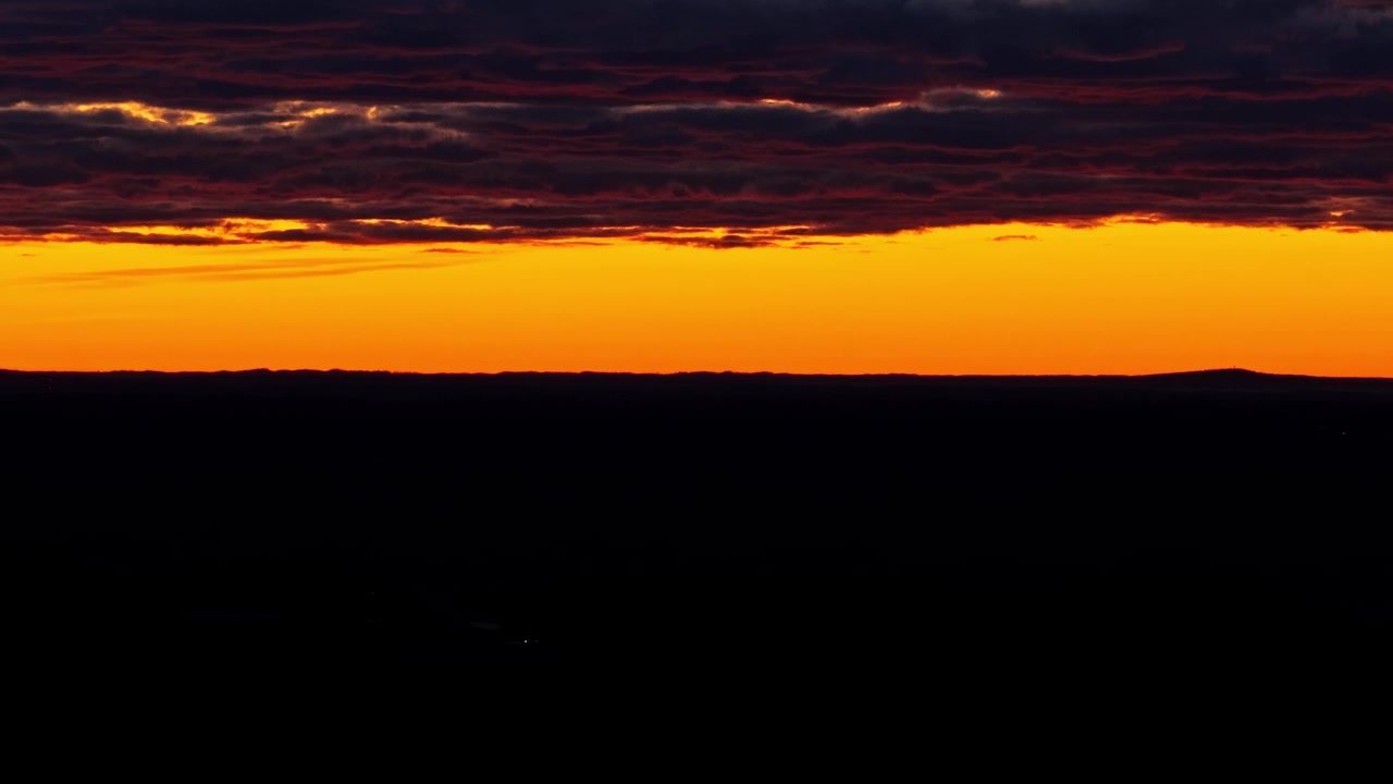 Pragtfuld levende solnedgang med mørke dramatiske skyer, der svæver over en mørk landskabssilhuet