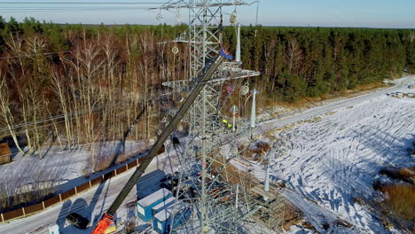 Vista-Aérea-Del-Trabajador-Que-Trabaja-En-La-Torre-De-Transmisión-En-El-Bosque-Durante-El-Día-De-Invierno-Con-Nieve