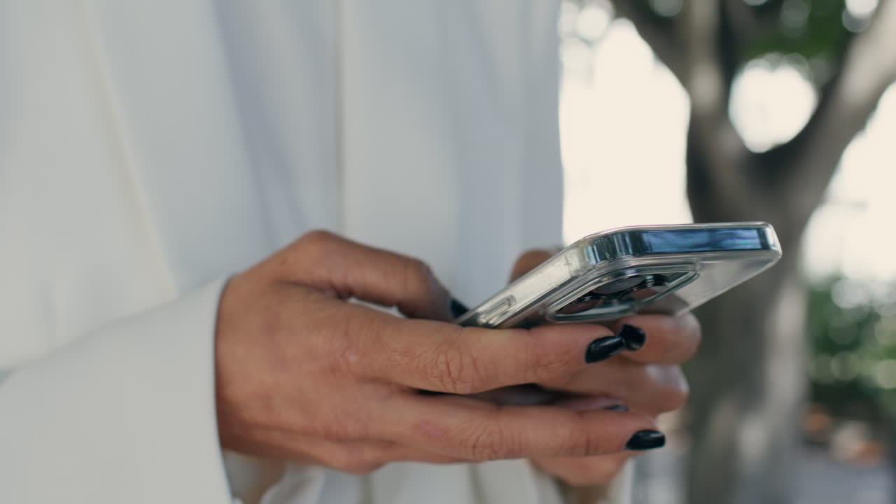 mujer de negocios manos mensajería teléfono en el parque de la ciudad de cerca. chica escribiendo sms.