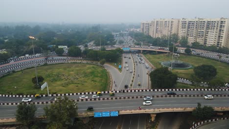 Aerial drone shot following the rush of vehicles on a Delhi flyover at sunset, with city lights beginning to glow.