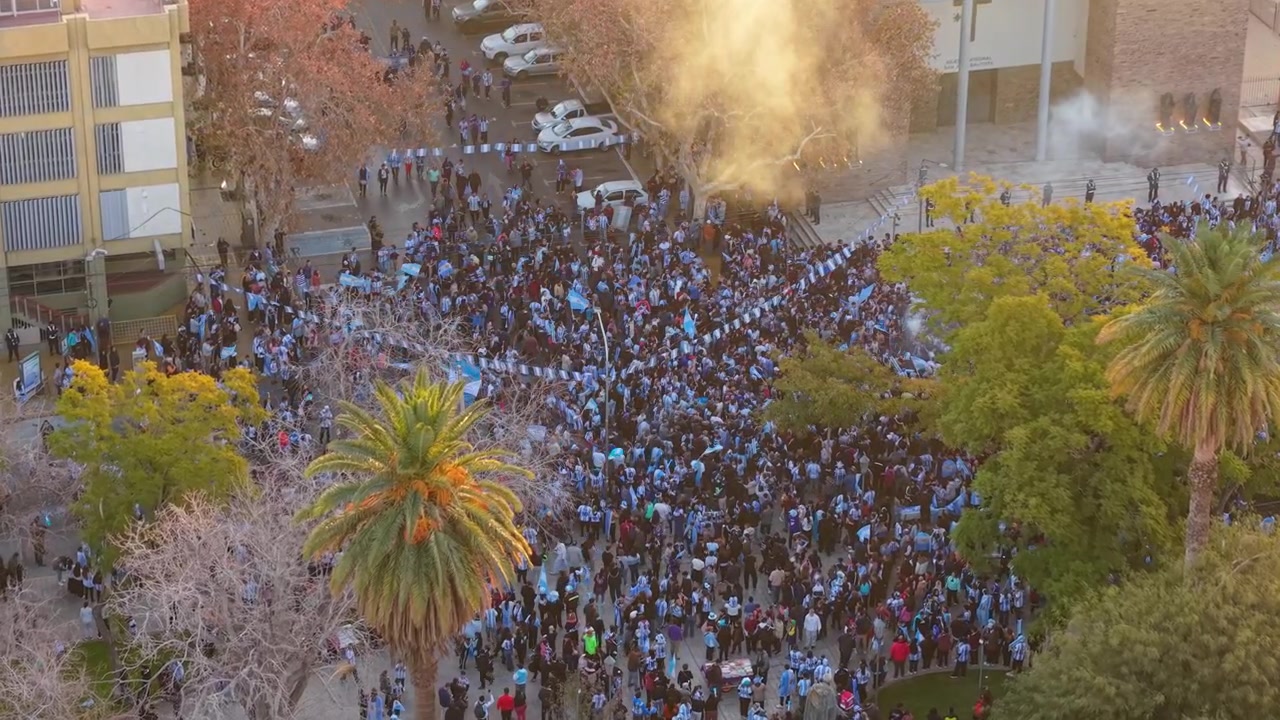 Luftfoto fra drone fanger en livlig folkemengde på Plaza 25 de Mayo, San Juan, Argentina, som vifter med flagg og feirer Argentinas seier i FIFA verdensmesterskap 2026 under gyllent sollys.