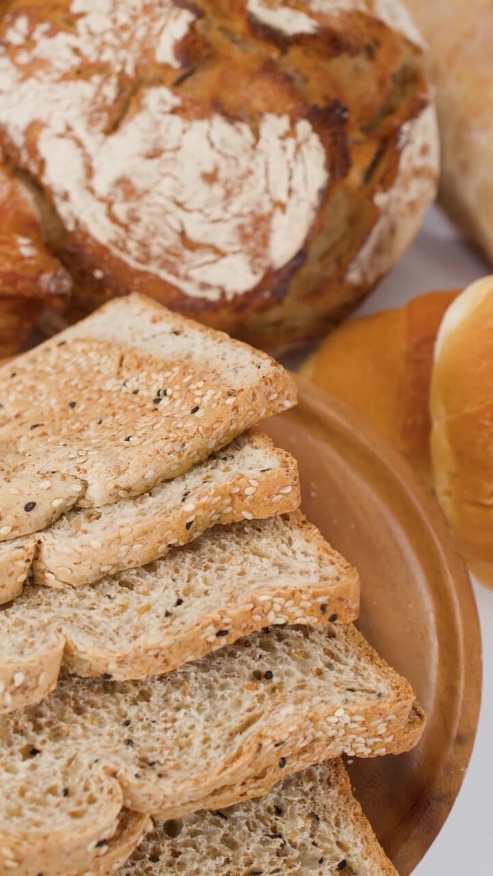 Close-up rotating view of sliced seeded bread, sourdough, and croissants on a wooden plate.