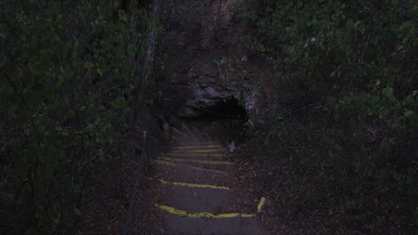 ascending drone shot above steps leading into a deep cave