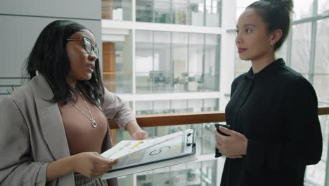 diverse female colleagues discussing documents in business center