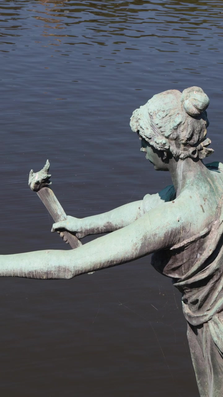 La telecamera circonda una statua classica in bronzo con torcia, con un fiume sullo sfondo, luce naturale del giorno e movimento fluido
