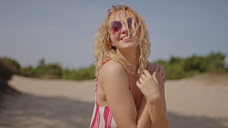 a beautiful blonde woman with curly hair smiles and laughs in slow motion while standing in sunny white sand dunes