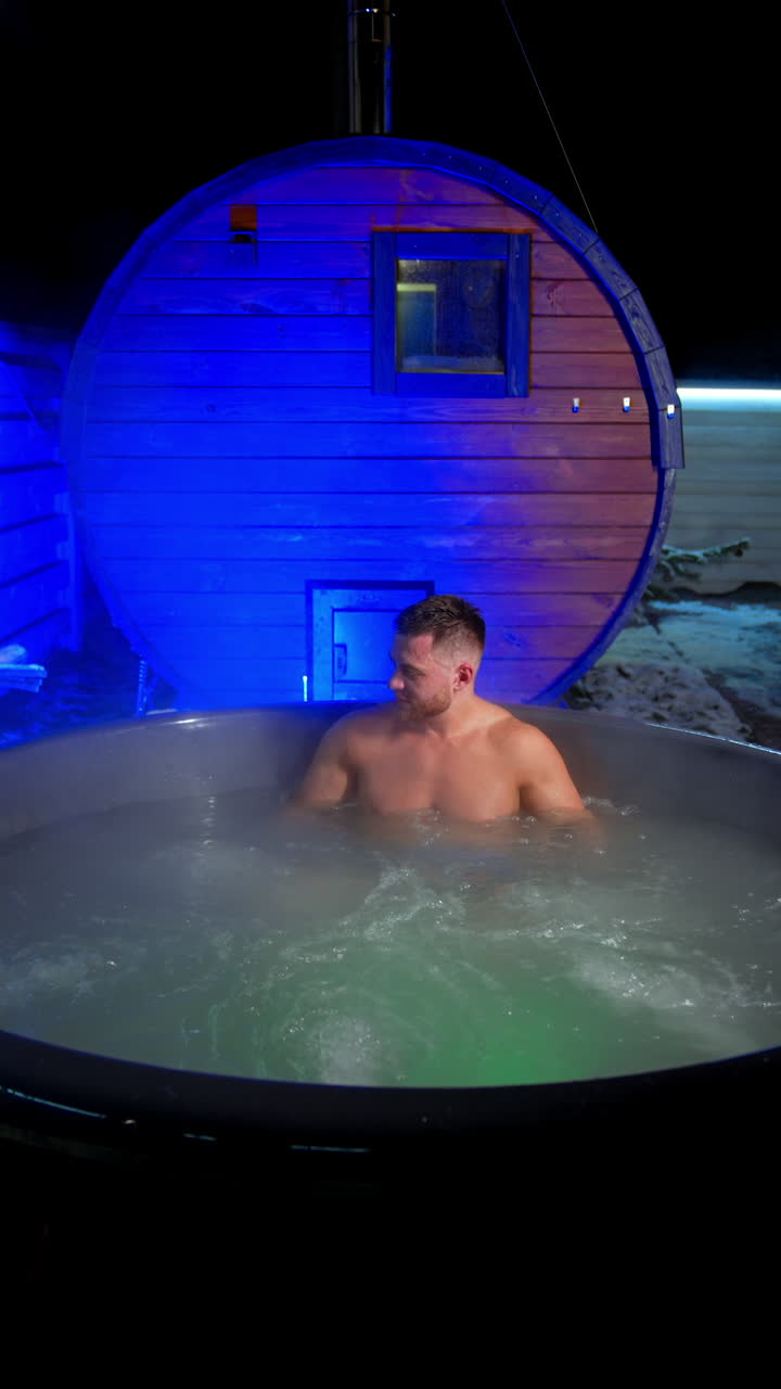 Young man sits in Jacuzzi his hands spread to the sides of the tub. Relaxation and spa procedures. Vertical video.