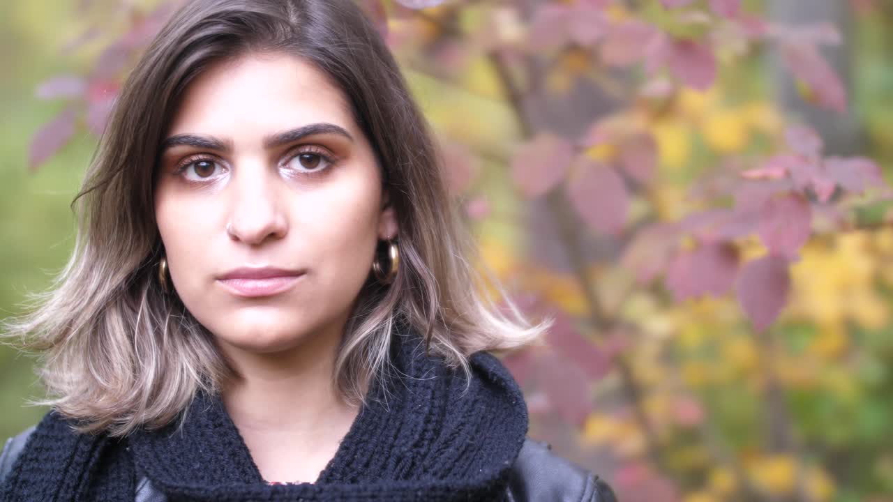 chica morena en el bosque de otoño se encuentra cerca de hojas amarillas y rojas y mira en la cámara - tiro cercano