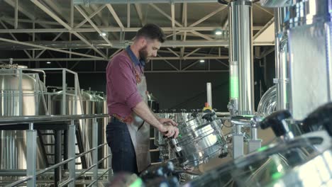 young male brewer wearing a leather apron supervise the process of beer fermentation at a modern brewery factory