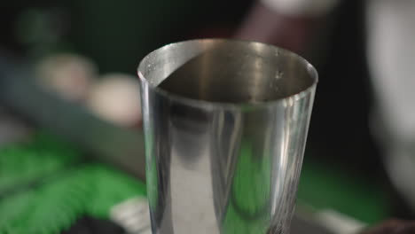 bartender pouring ice into cocktail shaker, preparing for drink mixing with modern bar tools, focused on drink creation in vibrant green-lit bar setting