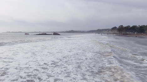 strong waves crashing ashore with broken pier and ship wreck in the background