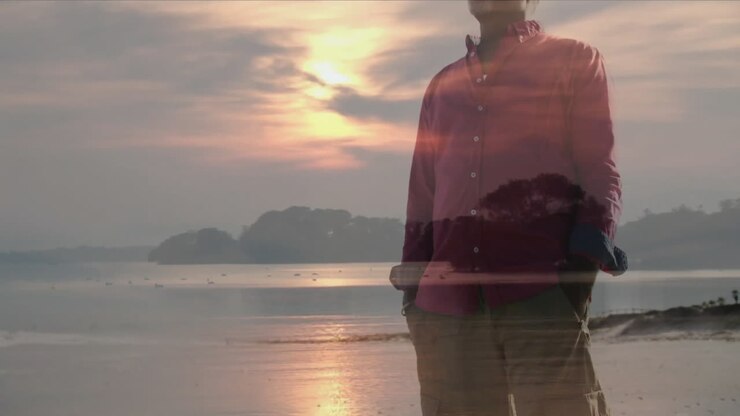 Hombre mayor de pie a orillas de un lago al atardecer, con un icono de corazón animado y una superposición de gráfico de bienestar.