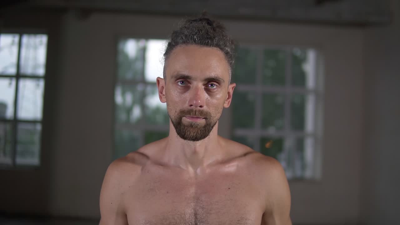 셔츠 없는 잘생긴 백인 남자의 클로즈업 초상화. 스타일리쉬한 드레드머리로 카메라를 보고 동기부여로 빈 홀 안에 서 있다.