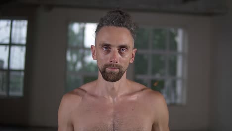 Closeup-portrait-of-shirtless-handsome-caucasian-man-with-stylish-dreadlocks-looking-at-camera-with-motivation-standing-in-the-empty-hall-indoors