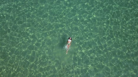 una mujer en bikini nada y chapotea en las verdes y brillantes aguas del mar egeo