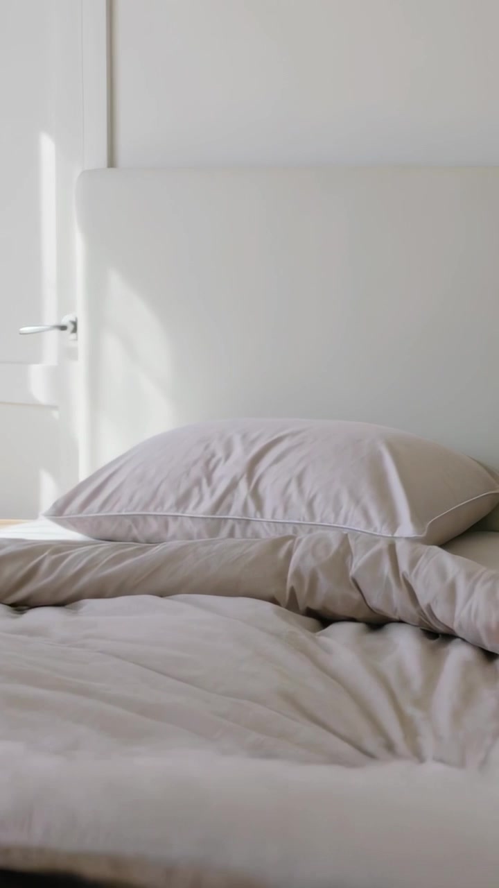 Vertical video: Pulling duvet, hand smoothing bed and tidying pillows in bedroom, with succulent
