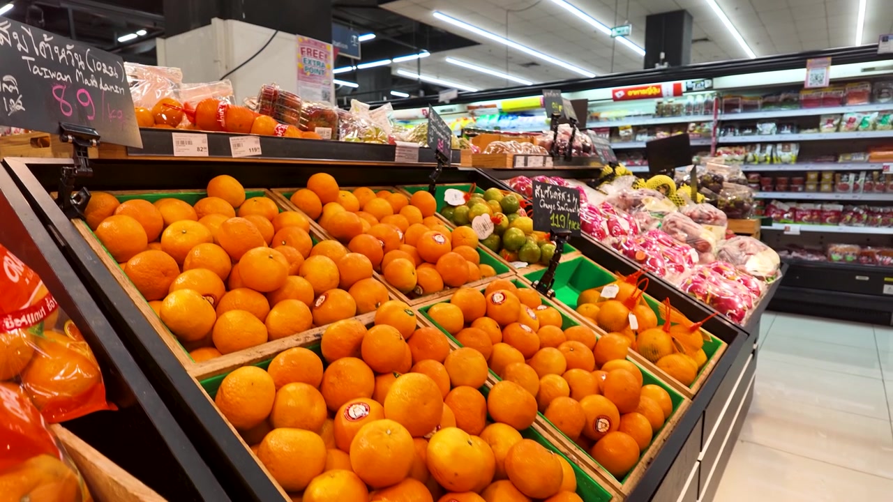 A person picks a fresh orange from a wooden crate in a bright grocery store.