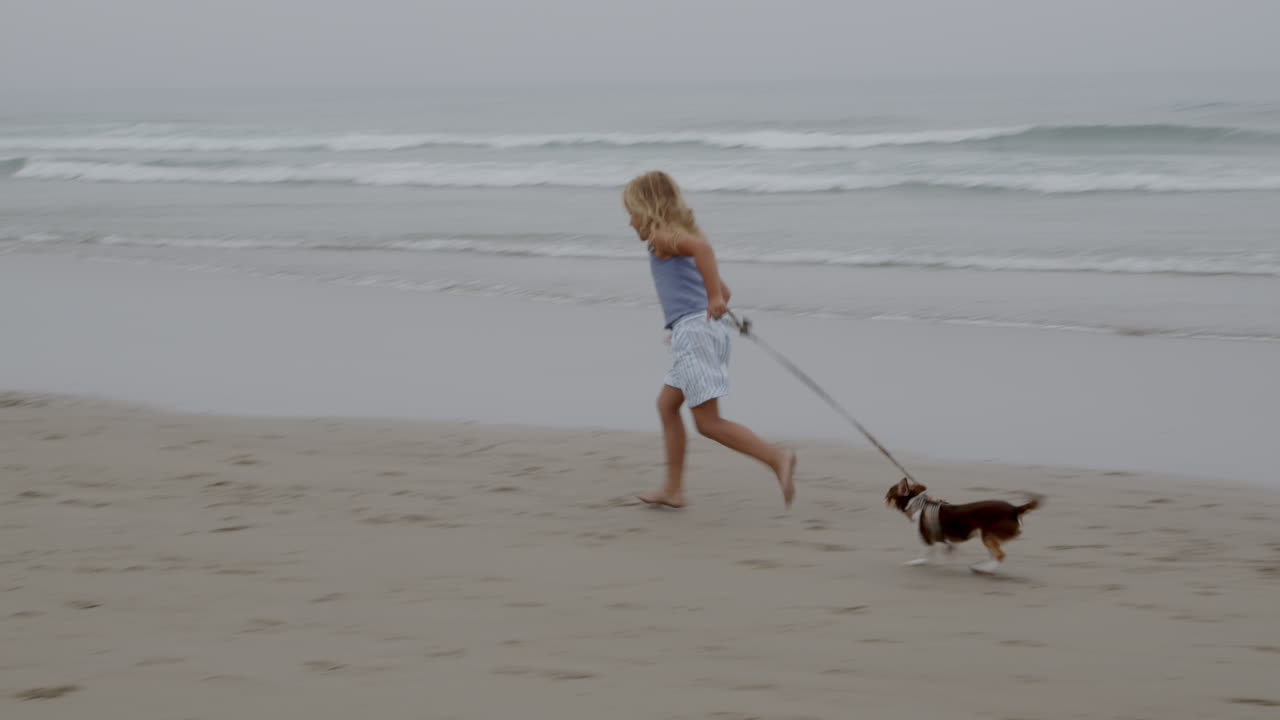 Ragazza e cane che corrono sulla spiaggia nella nebbia