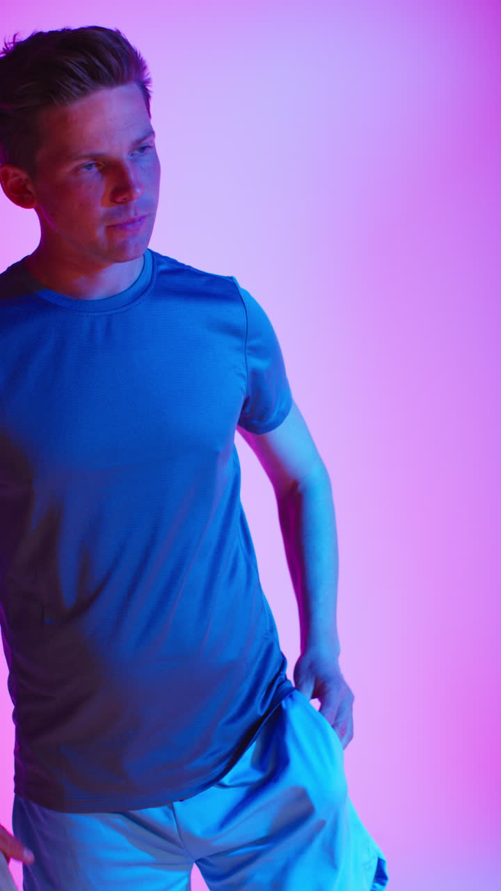 toma de estudio de video vertical de un jugador de tenis masculino con raqueta y pelota contra una iluminación mixta colorida de bajo tono