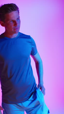 vertical video studio shot of male tennis player with racket and ball against low key colourful mixed lighting